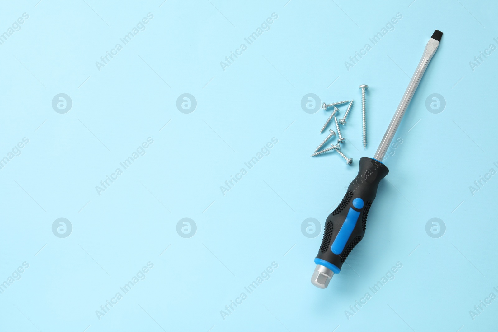 Photo of Screwdriver with black handle and screws on light blue background, flat lay. Space for text