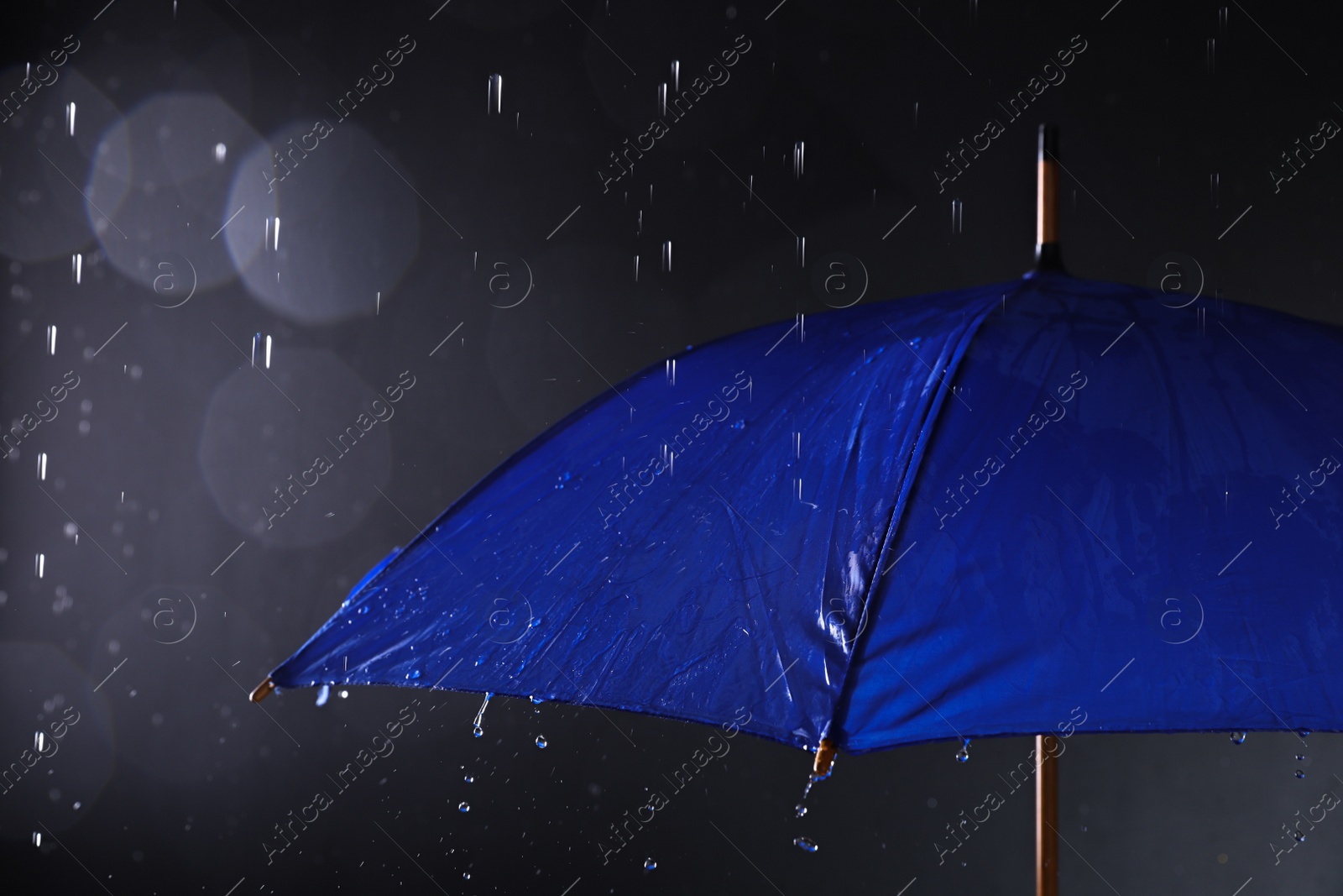 Photo of Bright umbrella under rain on dark background