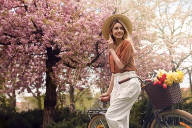 Photo of Beautiful young woman with bicycle and flowers in park on pleasant spring day. Space for text