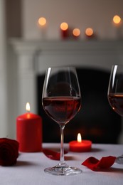 Glasses of red wine, burning candles and rose flower on grey table indoors. Romantic atmosphere