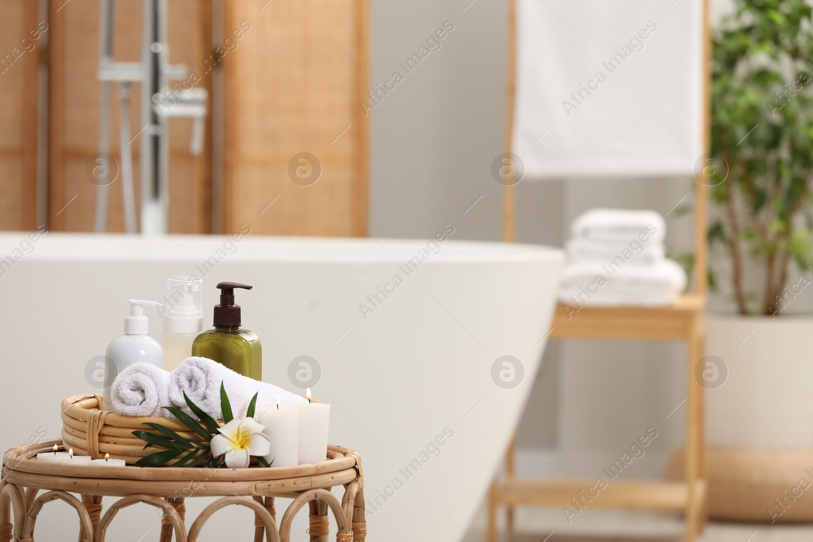 Photo of Spa products, burning candles, plumeria flower and tropical leaf on table in bathroom. Space for text