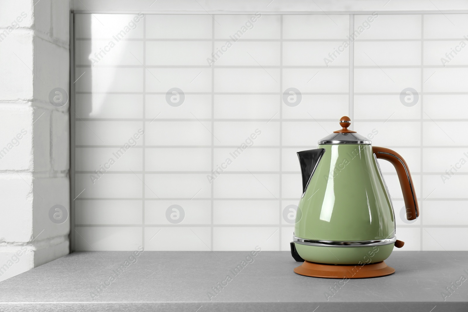 Photo of Stylish electric kettle on grey table against white wall, space for text. Tea preparation