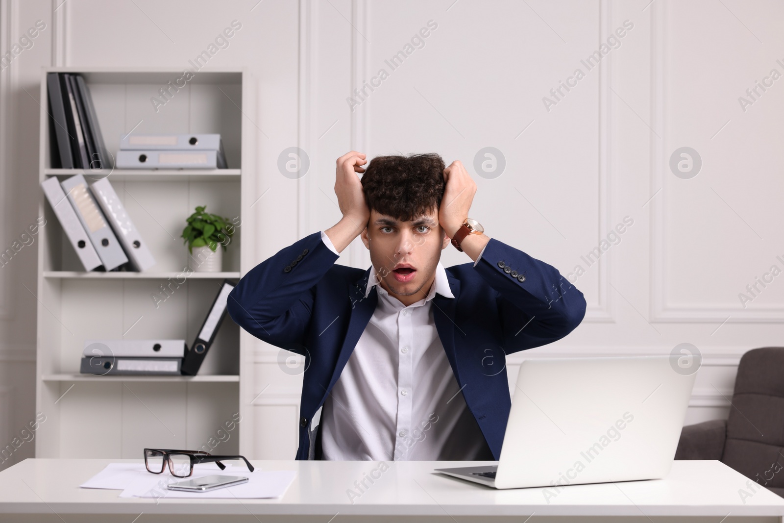 Photo of Emotional young man working at white table in office. Deadline concept