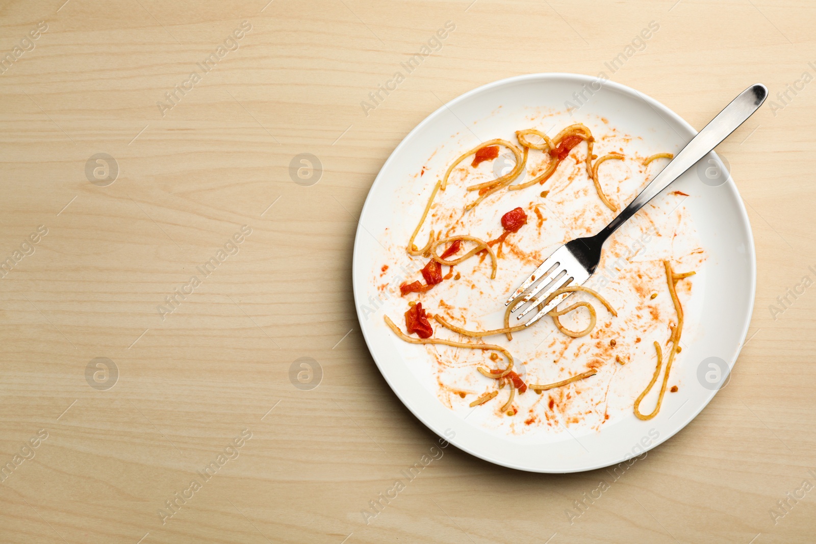 Photo of Dirty plate with food leftovers and fork on wooden background, top view. Space for text