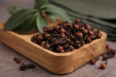 Photo of Wooden tray with aromatic cloves and green leaves on brown table, closeup
