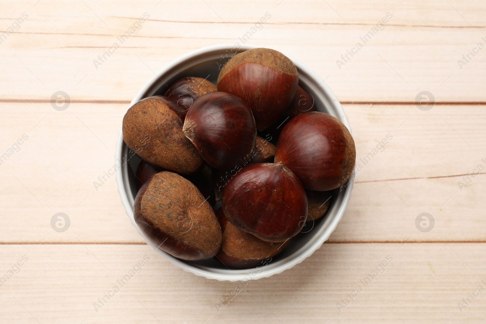 Photo of Sweet fresh edible chestnuts on light wooden table, top view