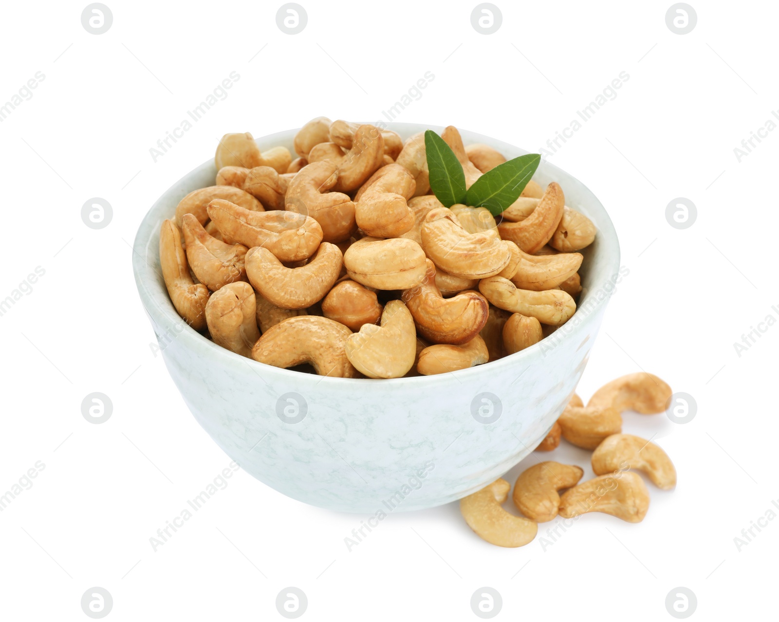 Photo of Bowl, tasty organic cashew nuts and green leaves isolated on white