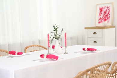 Beautiful table setting with green branches in vases and burning candles in dining room