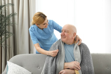 Photo of Nurse covering elderly man with blanket indoors. Assisting senior people