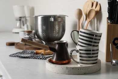 Cezve, cups and other cooking utensils on countertop in kitchen