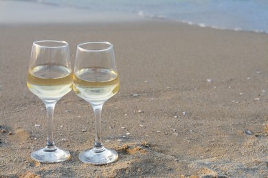 Glasses of tasty wine on sandy beach, space for text