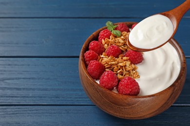 Photo of Eating tasty yogurt with raspberries and muesli from bowl on blue wooden table. Space for text
