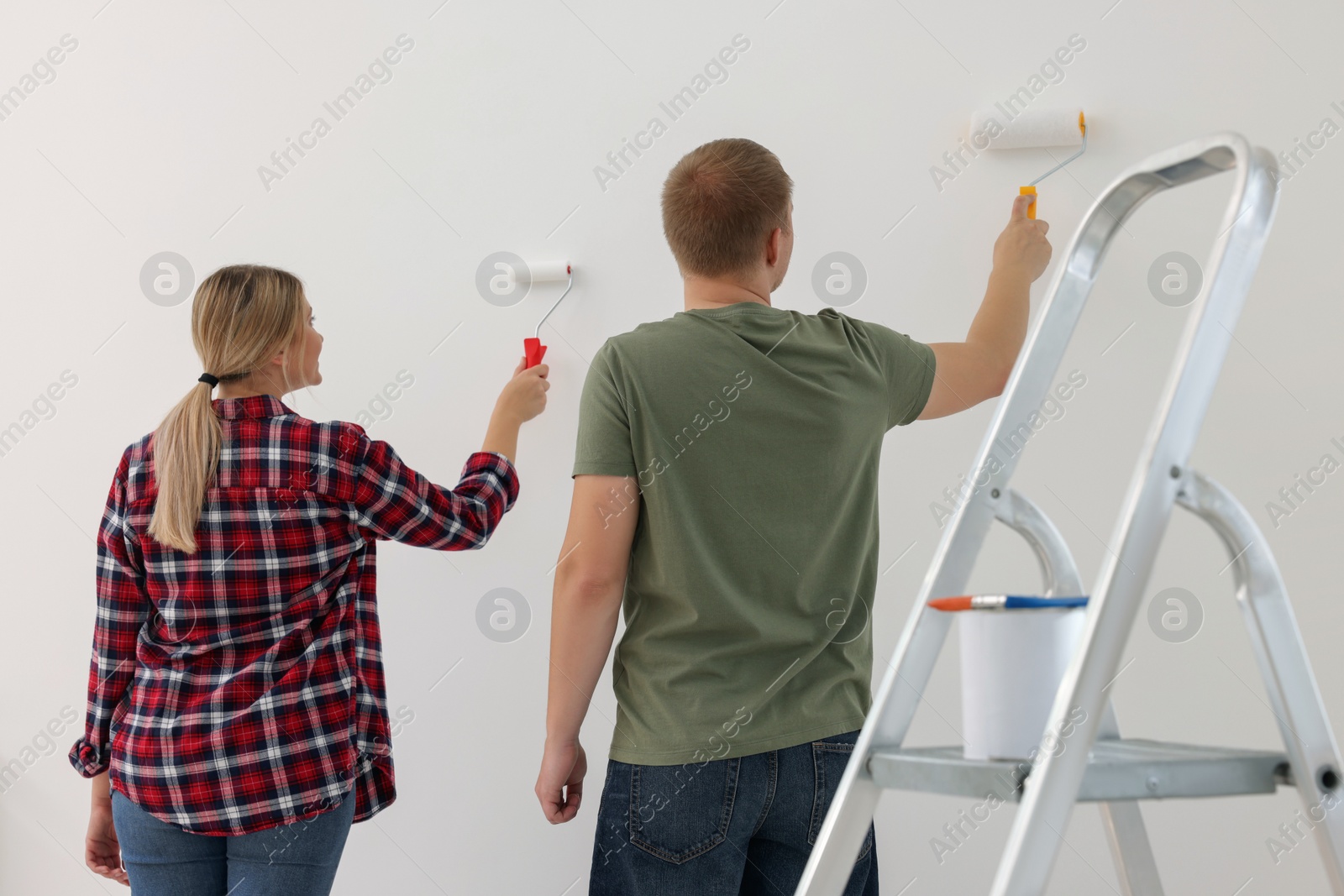 Photo of Couple painting wall in apartment during repair, back view