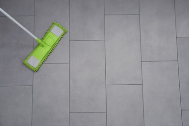 Photo of Cleaning grey tiled floor with microfiber mop, top view. Space for text