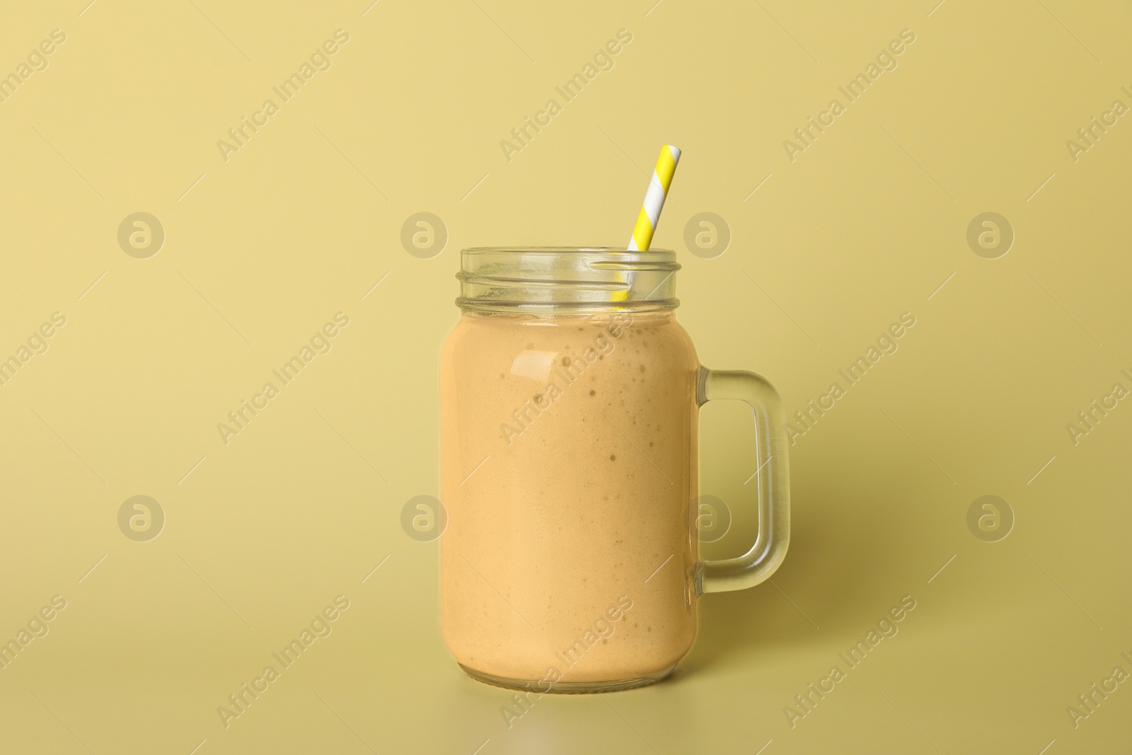 Photo of Mason jar of tasty smoothie with straw on beige background