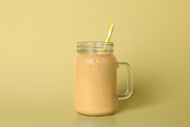 Mason jar of tasty smoothie with straw on beige background