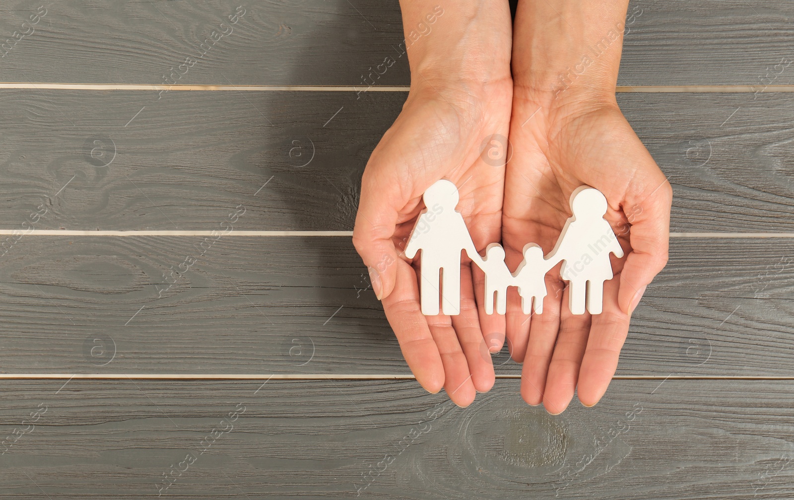 Photo of Woman holding figures of family in hands on grey wooden background, top view
