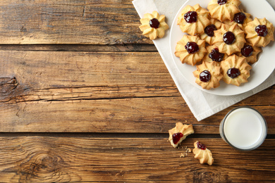 Photo of Tasty shortbread cookies with jam and milk on wooden table, flat lay. Space for text