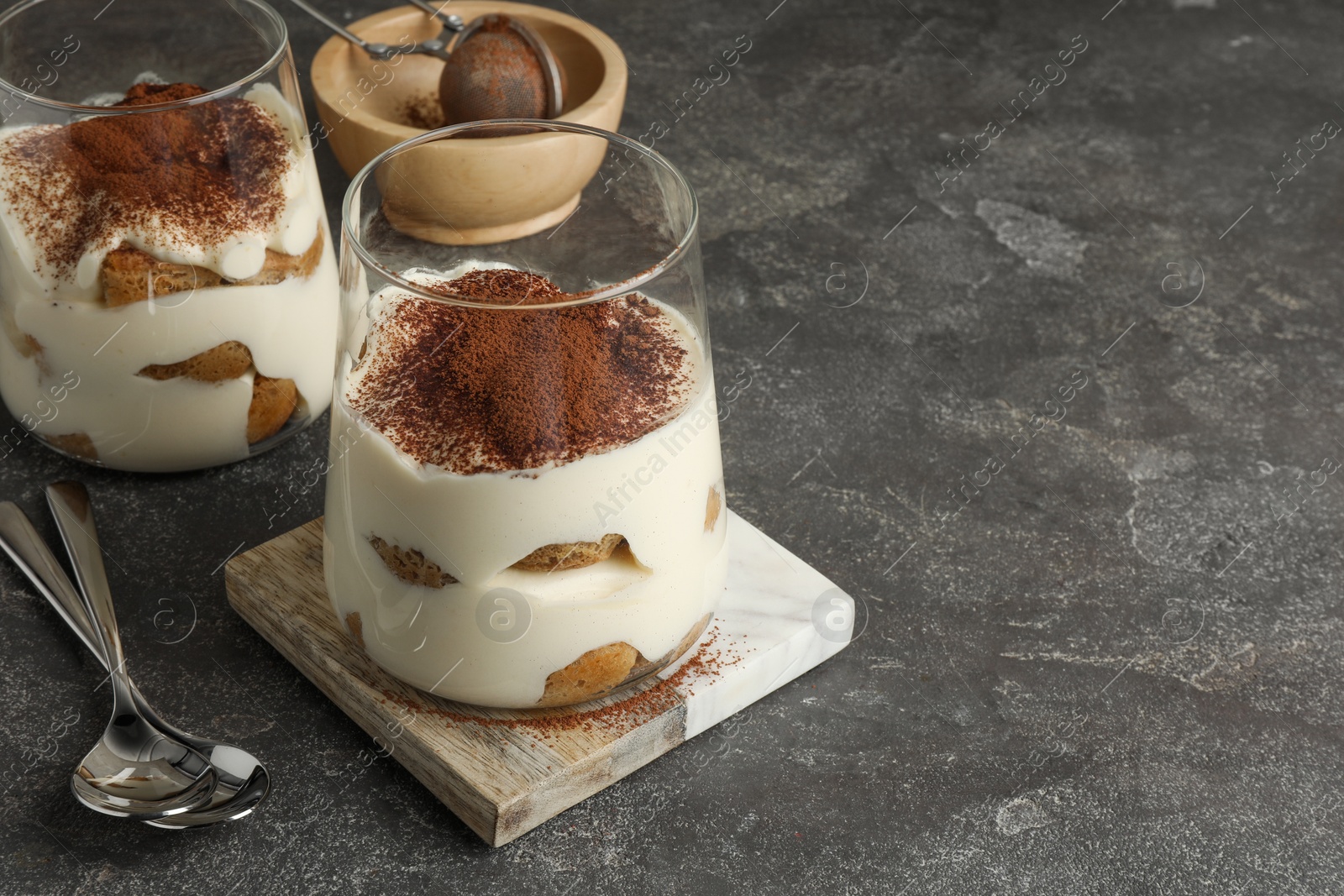 Photo of Delicious tiramisu in glasses on grey table. Space for text