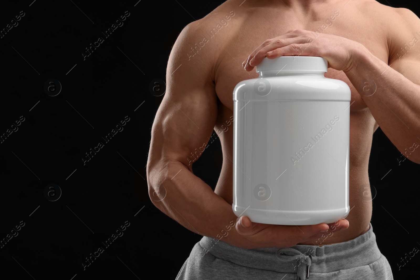 Photo of Young man with muscular body holding jar of protein powder on black background, closeup. Space for text