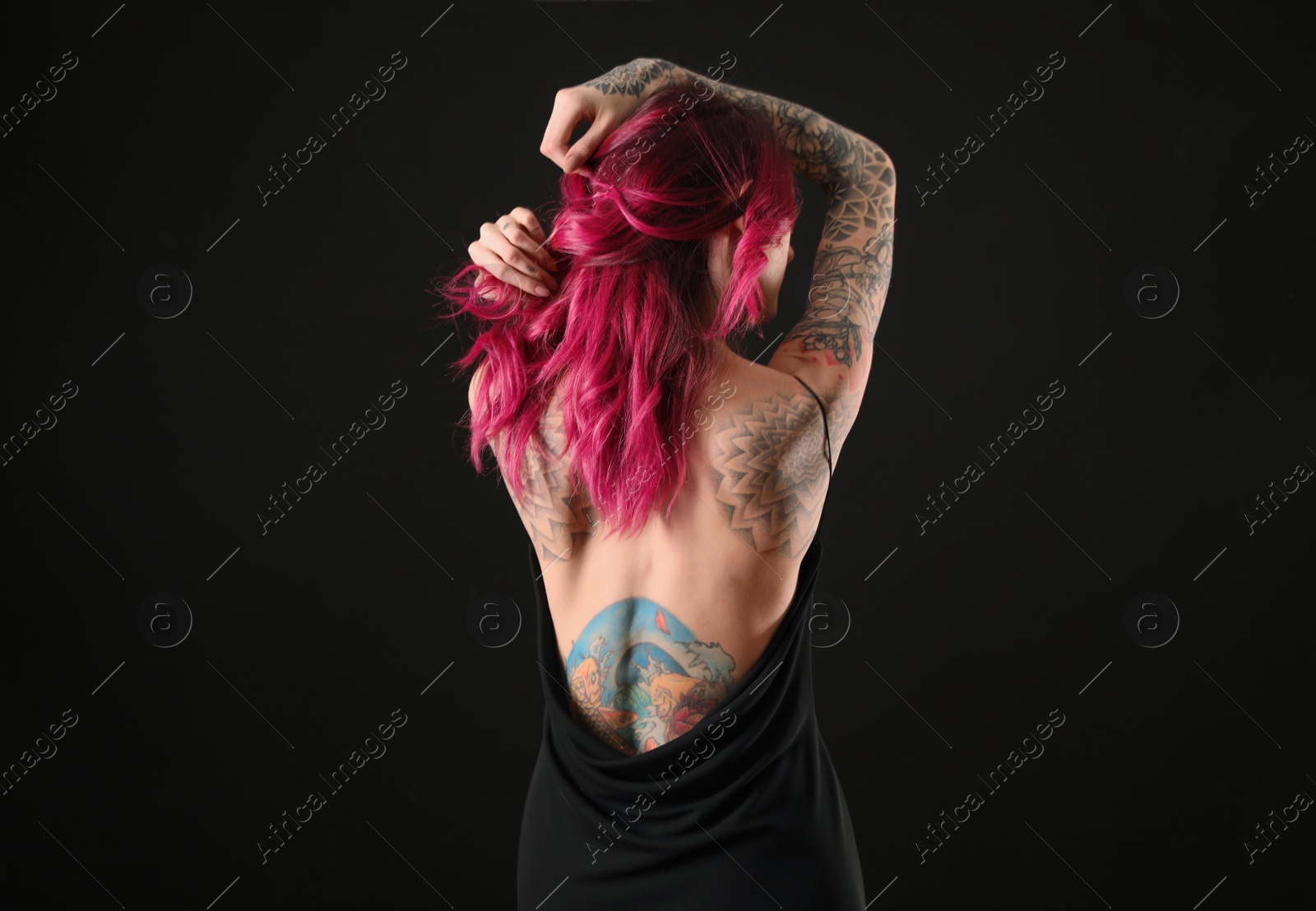 Photo of Beautiful woman with tattoos on body against black background, back view