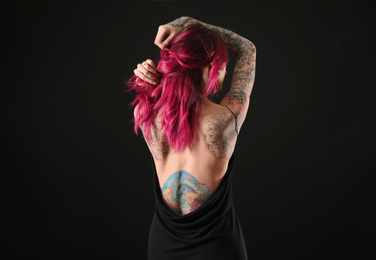 Photo of Beautiful woman with tattoos on body against black background, back view
