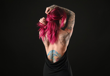 Beautiful woman with tattoos on body against black background, back view