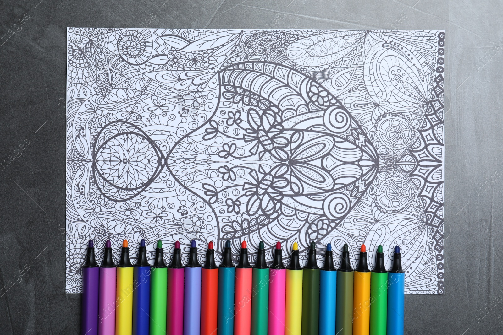 Photo of Antistress coloring page and felt tip pens on grey table, flat lay