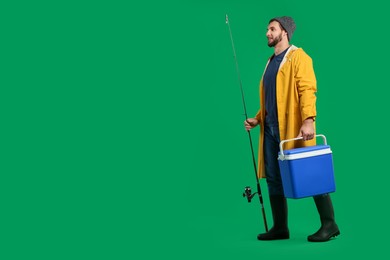 Photo of Fisherman with fishing rod and cool box on green background, space for text