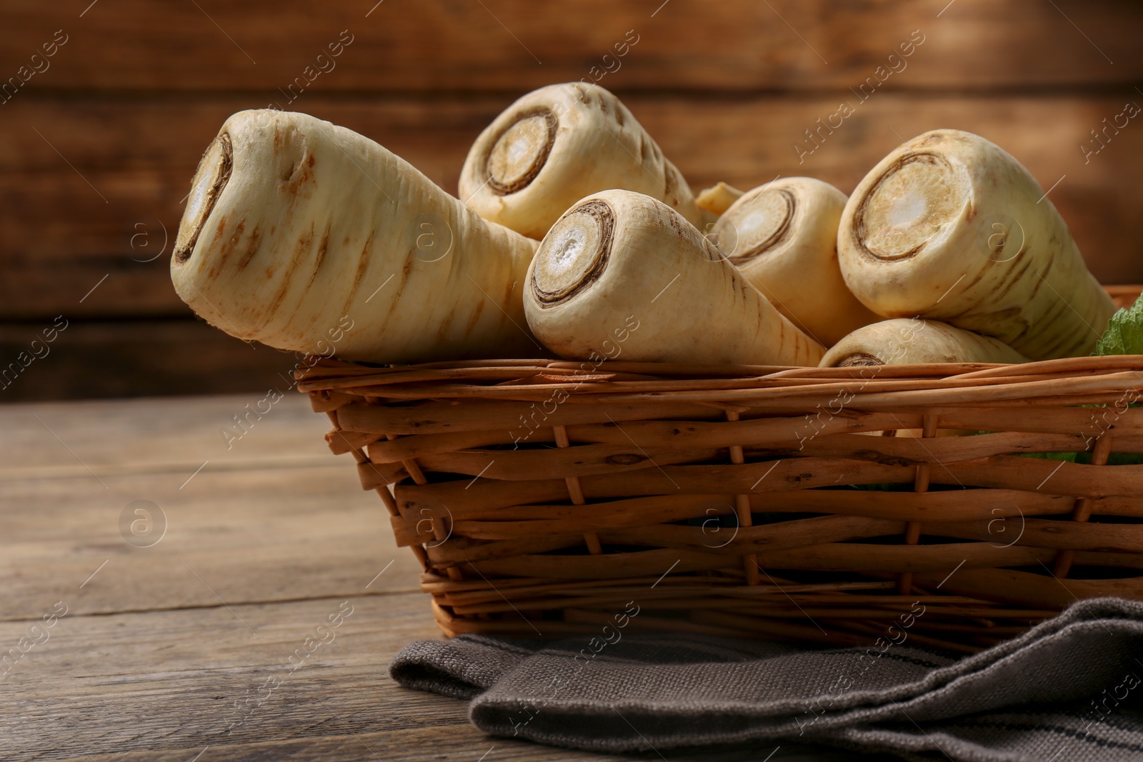 Photo of Wicker basket with delicious fresh ripe parsnips on wooden table, closeup