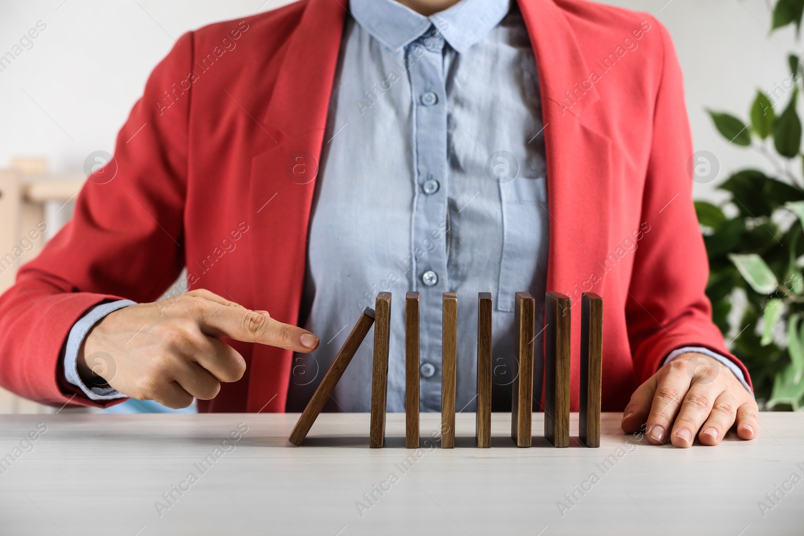 Photo of Woman causing chain reaction by pushing domino tile at table, closeup