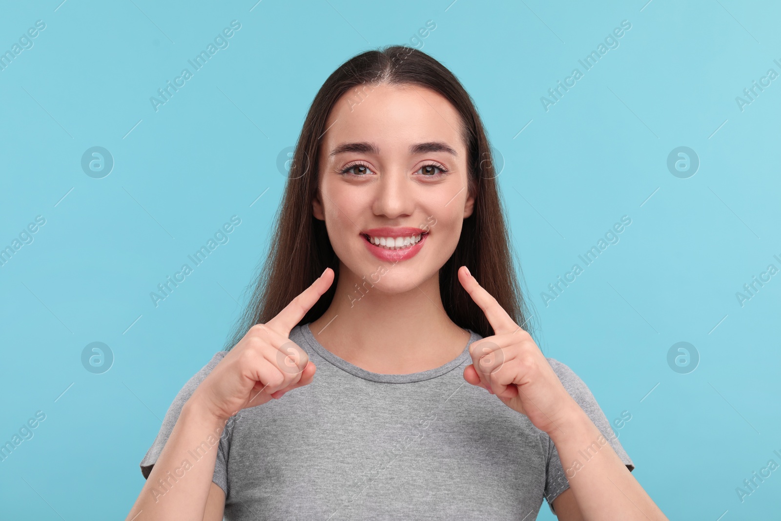 Photo of Young woman pointing at her clean teeth and smiling on light blue background