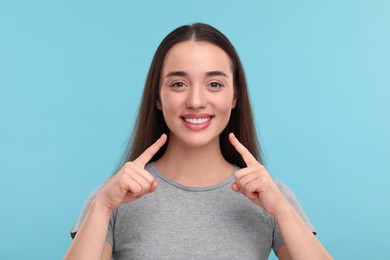 Young woman pointing at her clean teeth and smiling on light blue background