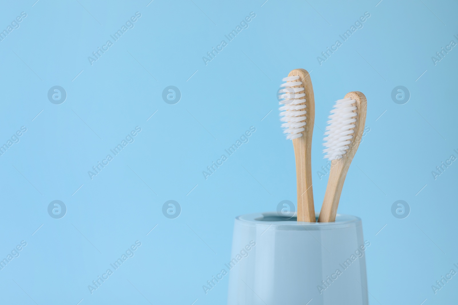 Photo of Bamboo toothbrushes in holder on light blue background, space for text