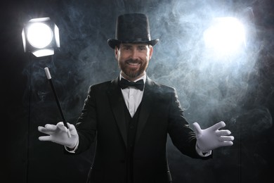 Photo of Happy magician with wand in smoke on stage
