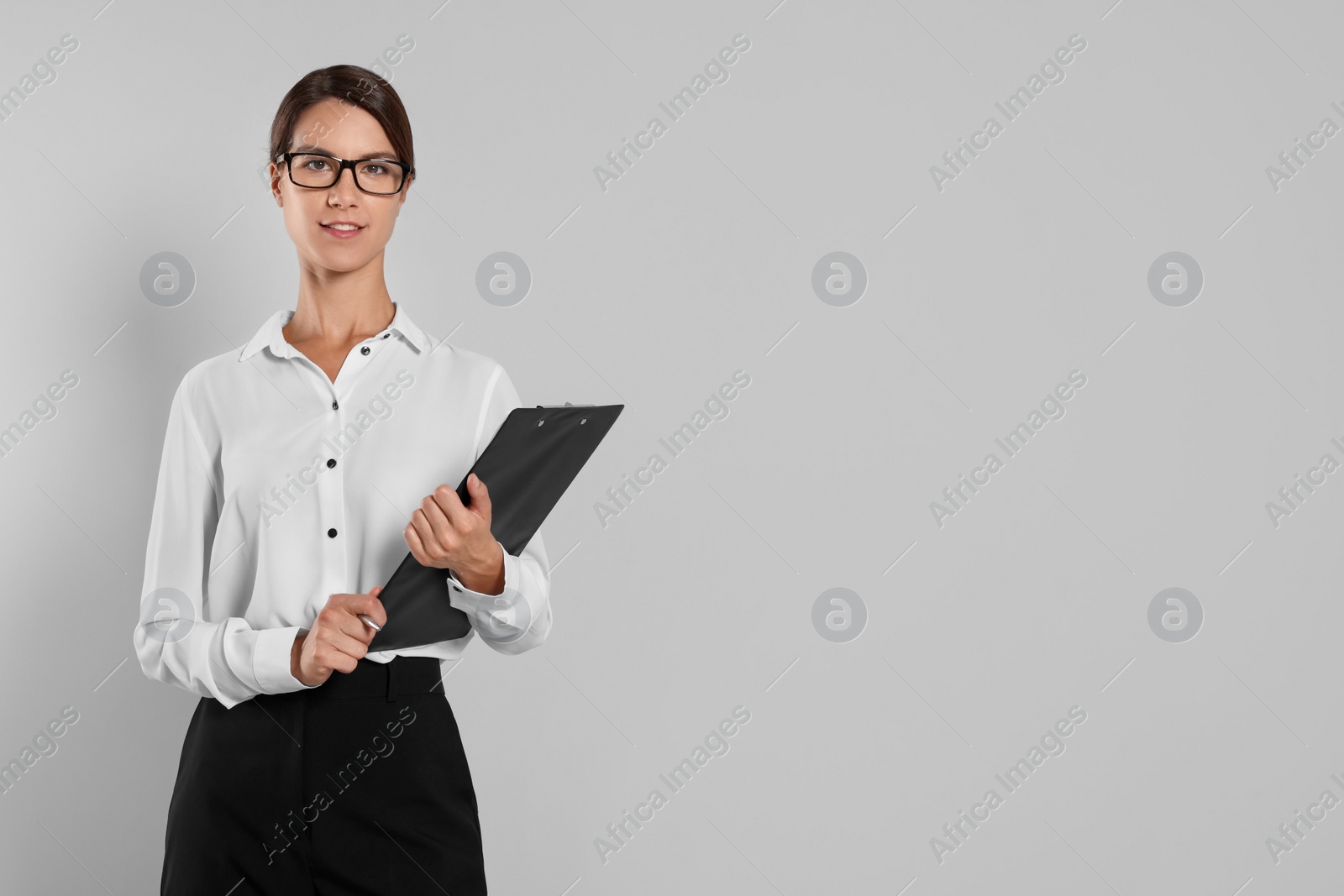 Photo of Young secretary with clipboard and pen on light grey background, space for text