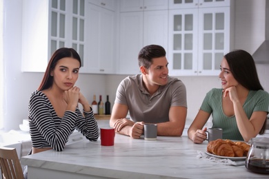 Unhappy woman feeling jealous while couple spending time together in kitchen