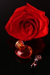 Photo of Heart shaped bottle of love potion, key and red rose on mirror surface