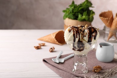 Photo of Glass dessert bowl of tasty ice cream with chocolate topping and nuts served on white wooden table. Space for text