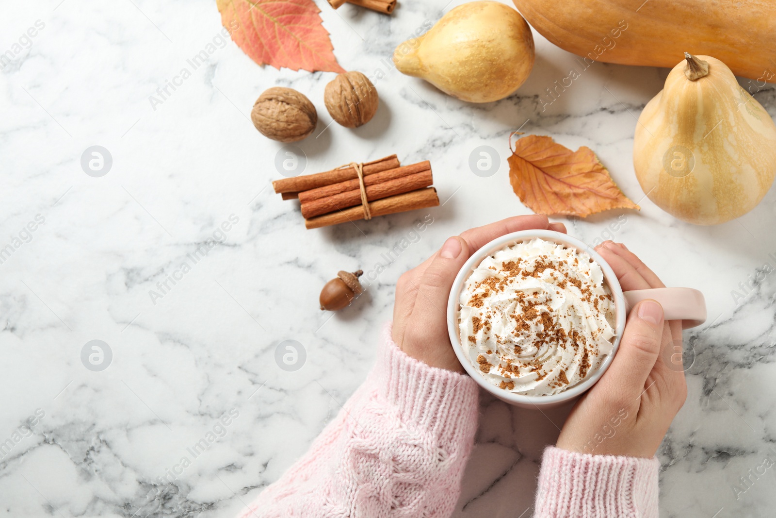 Photo of Woman with cup of tasty pumpkin spice latte at white marble table, top view. Space for text