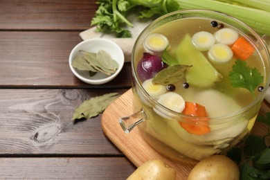 Glass pot with tasty bouillon and different ingredients on wooden table, space for text