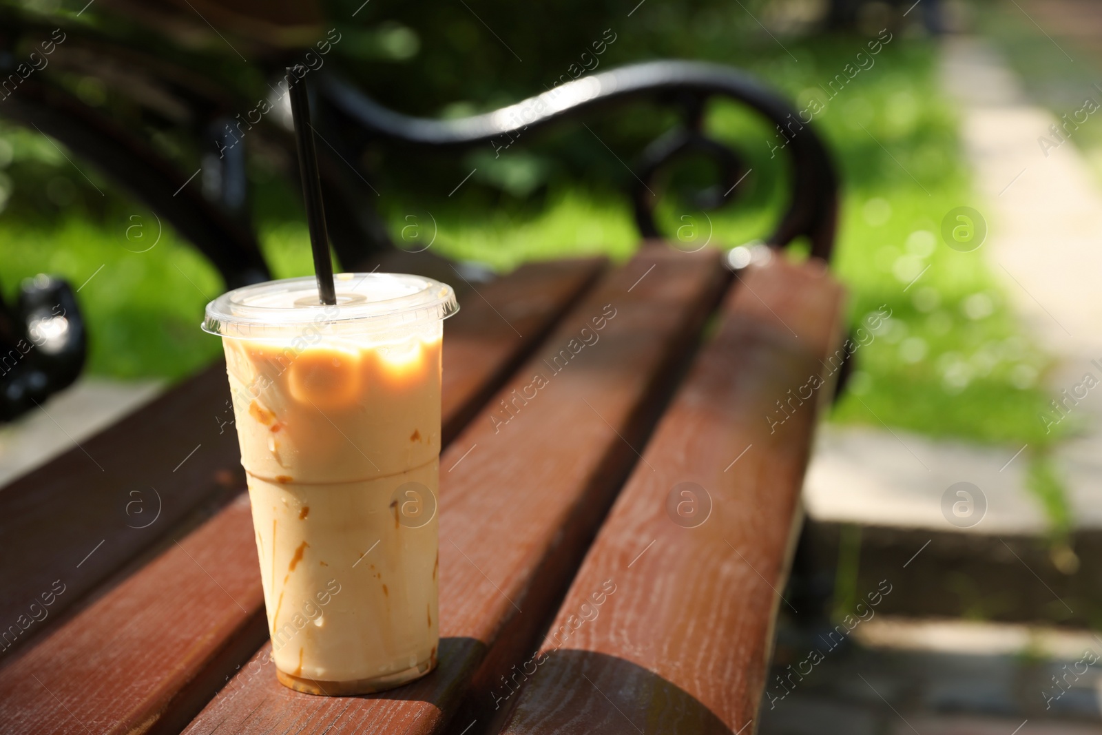 Photo of Takeaway plastic cup with cold coffee drink and straw on wooden bench outdoors, space for text