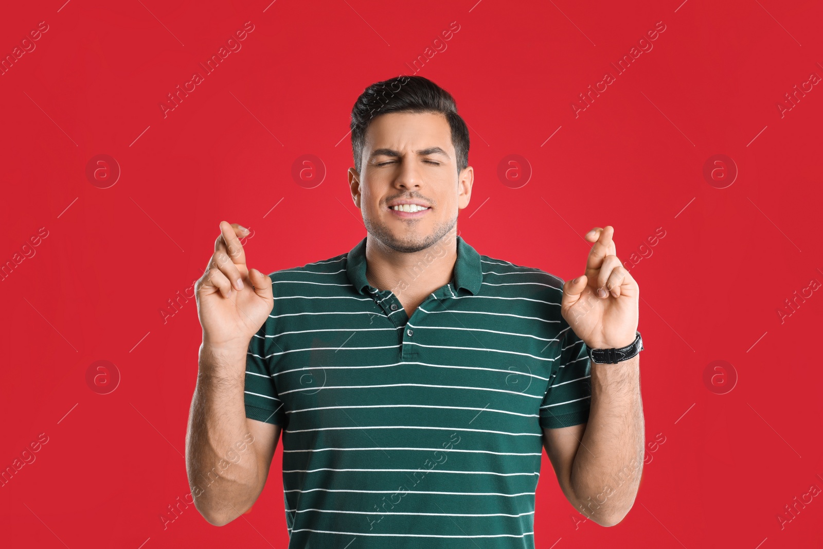 Photo of Man with crossed fingers on red background. Superstition concept