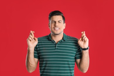 Photo of Man with crossed fingers on red background. Superstition concept