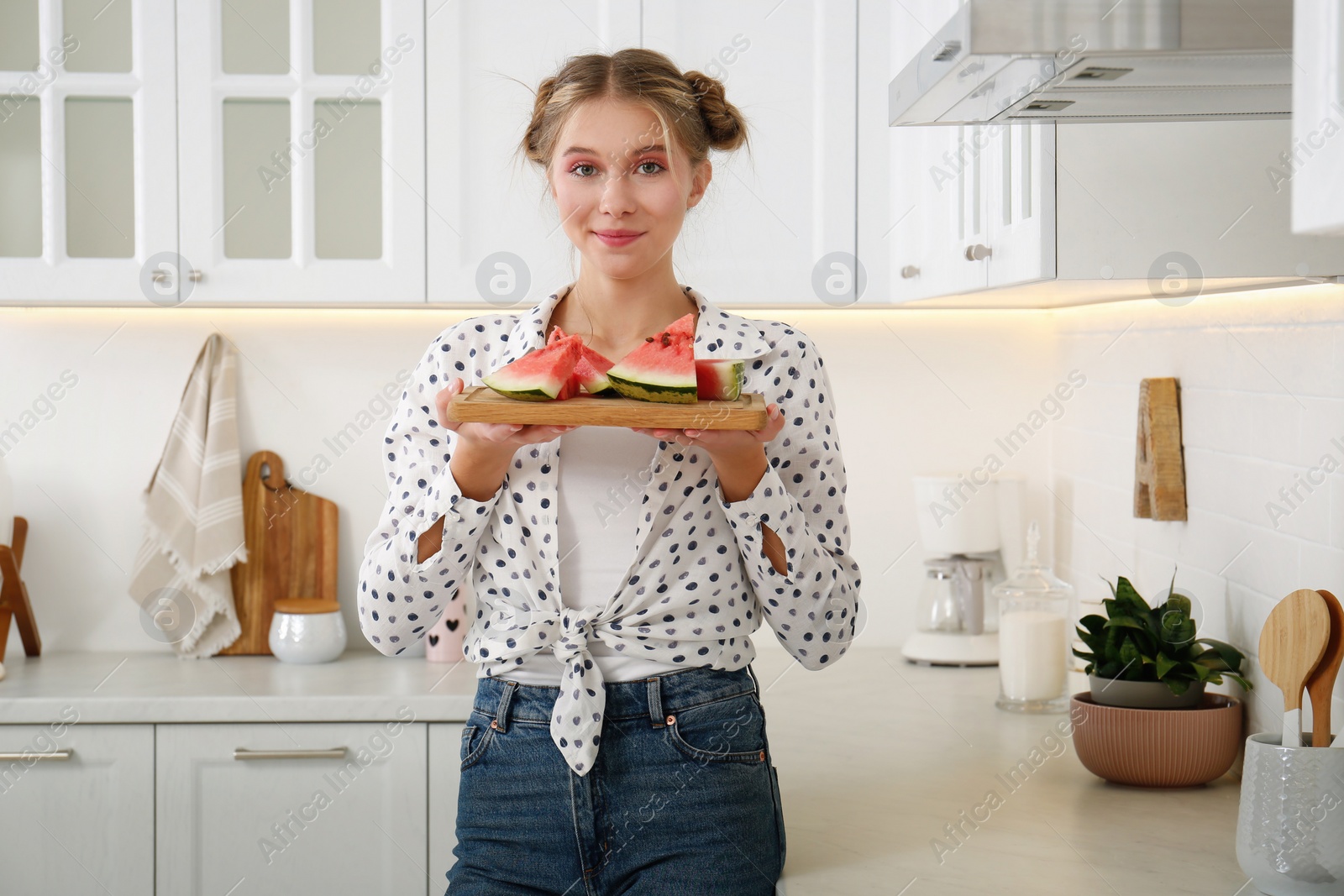 Photo of Beautiful teenage girl with slices of watermelon near countertop in kitchen