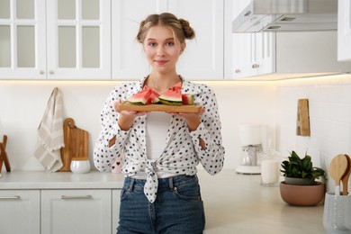 Photo of Beautiful teenage girl with slices of watermelon near countertop in kitchen