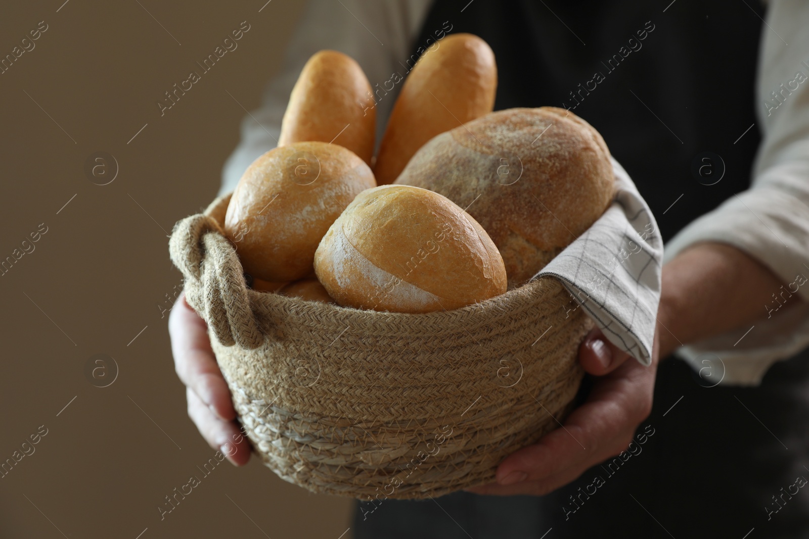 Photo of Man holding wicker basket with different types of bread on brown background, closeup