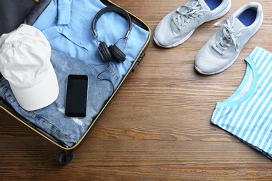 Flat lay composition with suitcase, clothes and space for text on wooden background