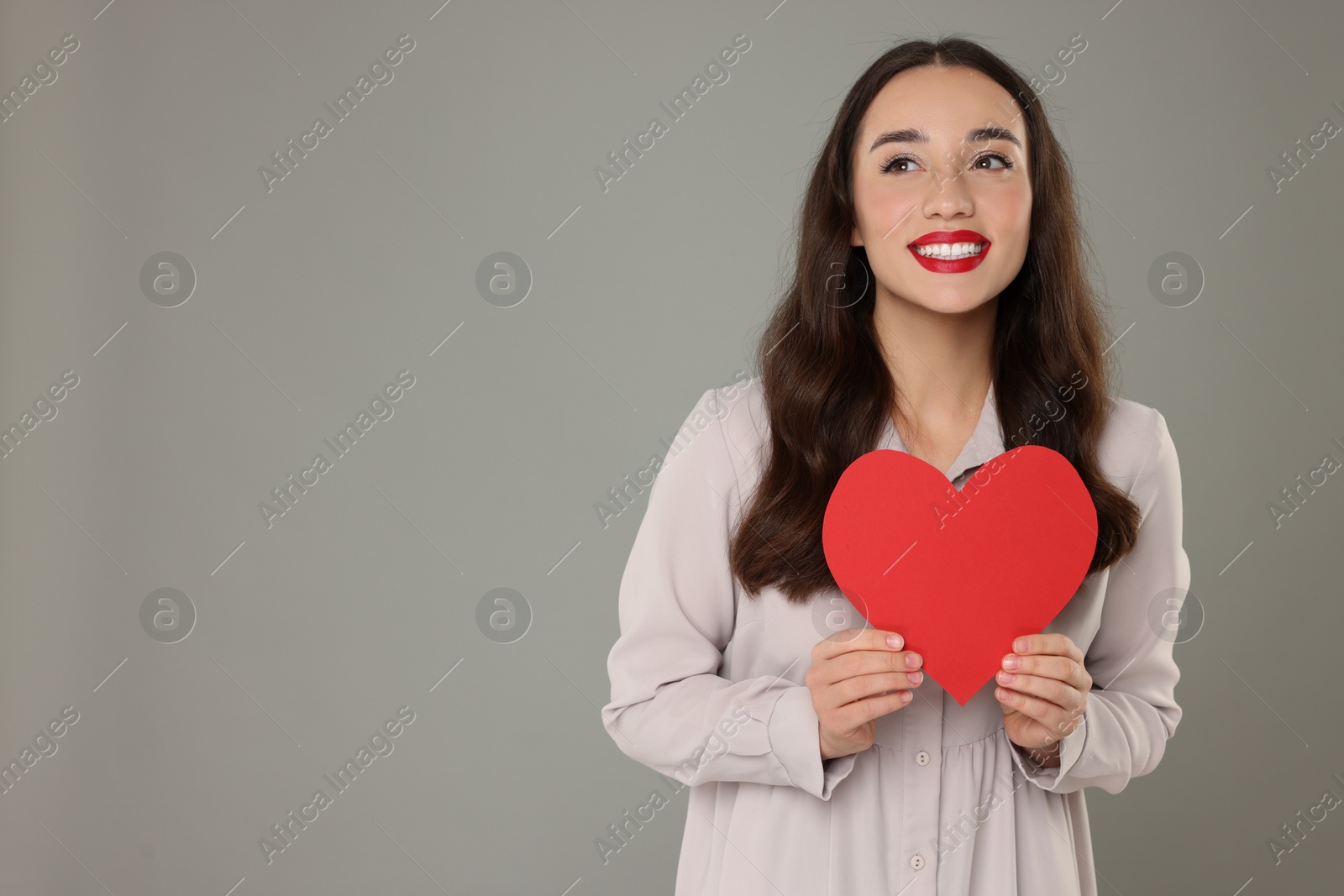 Photo of Beautiful young woman with paper heart on grey background, space for text