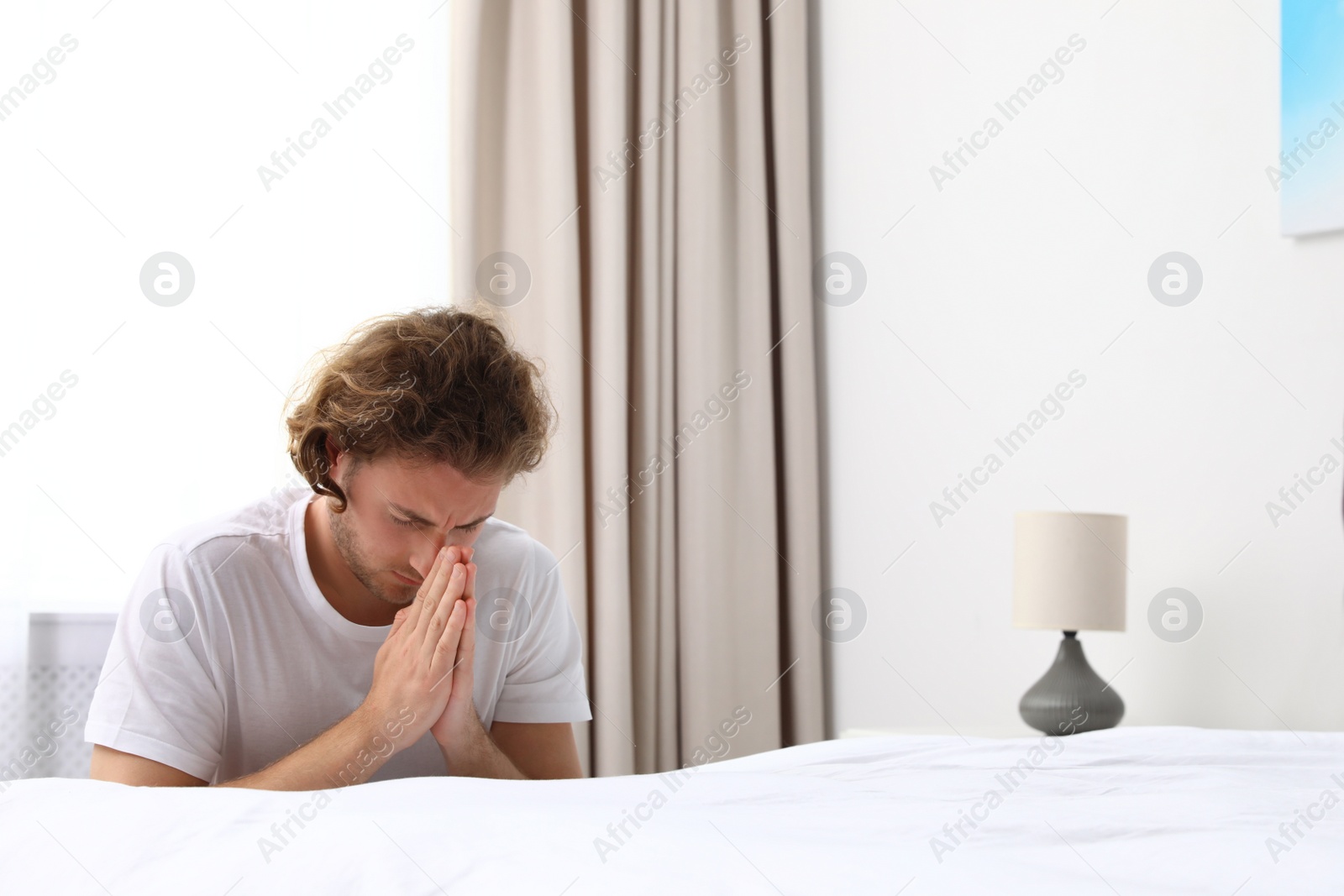 Photo of Handsome young man saying bedtime prayer at home. Space for text